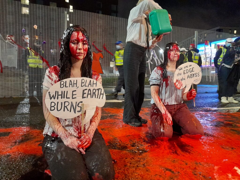 Two women kneel outside COP26 covered in fake blood.