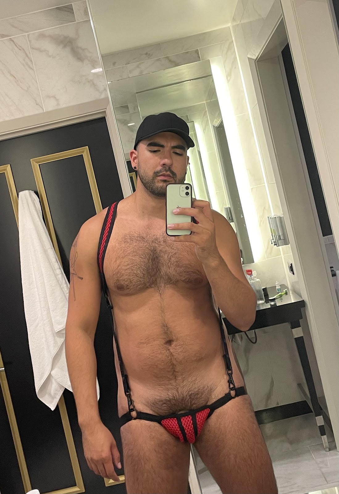 hairy gay muscle slut posing in red and black harness in hotel mirror