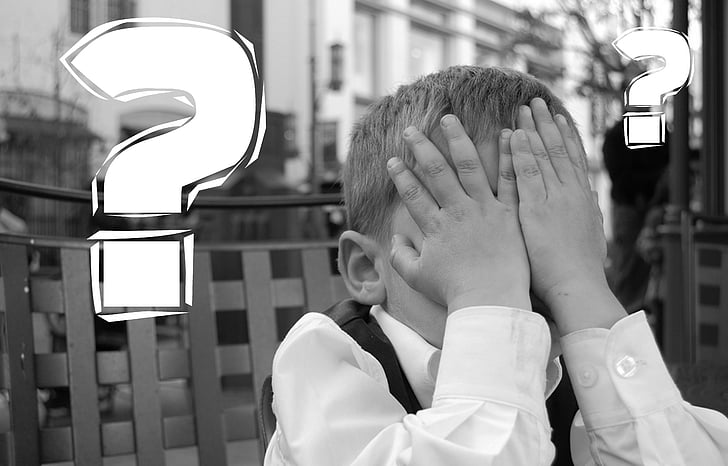Black and white image of small child covering eyes with hands, with question marks by his head