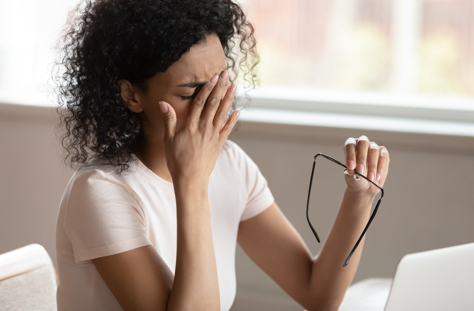 A woman taking off her glasses and rubbing her eyes due to digital eye strain