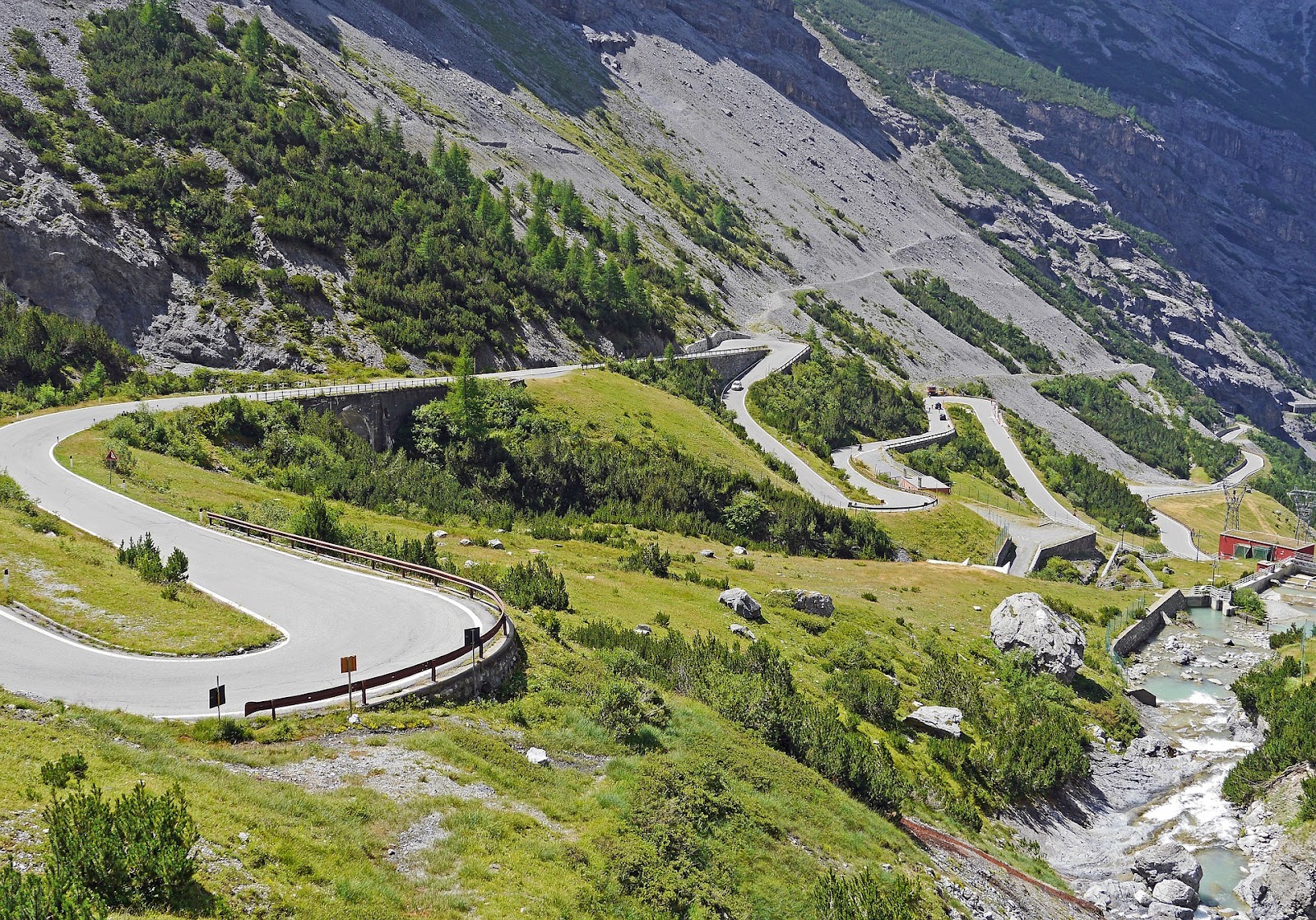 stelvio pass touge twisty uphill paved road in alps surrounded by green grass and stones