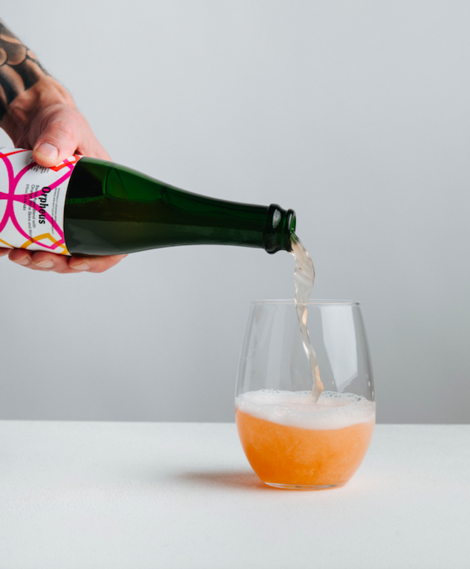 A bottle of Orpheus being poured into a round, stemless glass