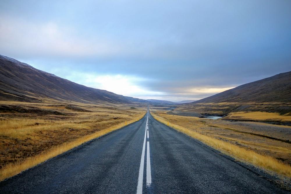 landscape photography of black asphalt road with white line surrounded by brown grass field during daytime