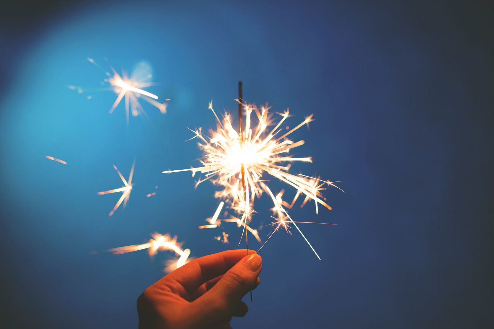 A persons hand holding a lit sparkler in front of a blue backdrop