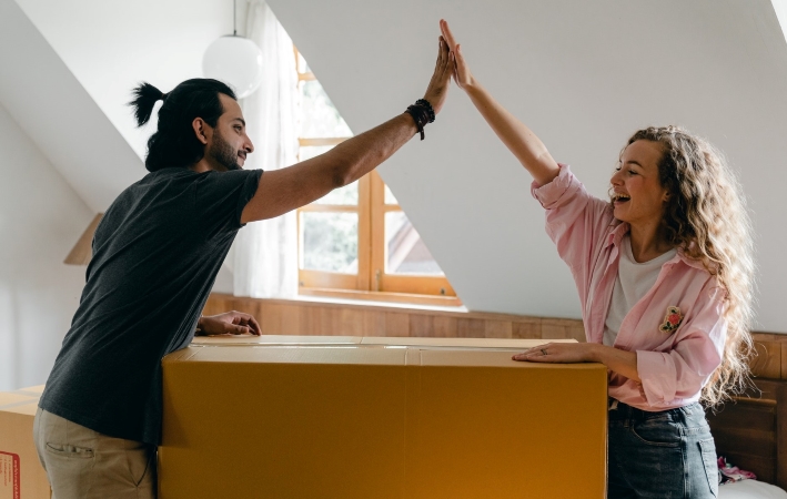 A man and woman give each other a high-five after packing up the last of their moving boxes. 