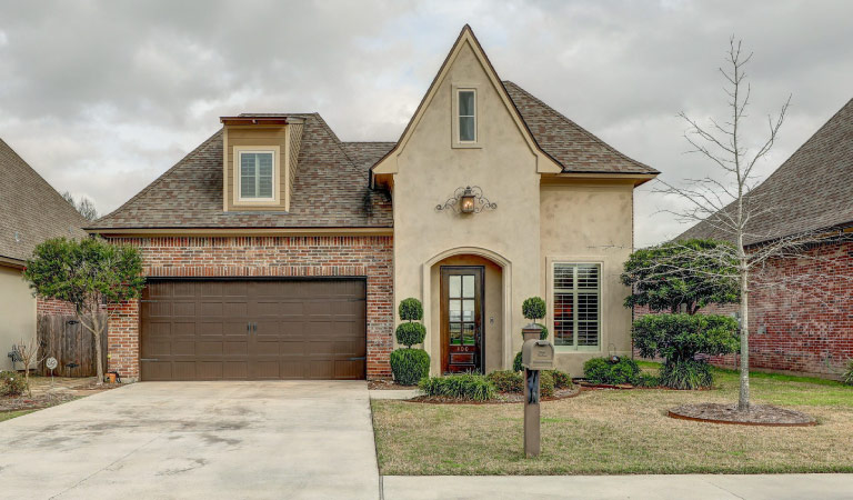 A unique, brick and stucco home in Youngsville, Louisiana. The landscaping in the front yard is masterfully done and an old-fashioned sconce hangs above the entrance. 