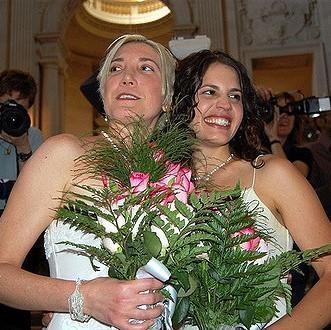 Una novia y una novia vestidas con vestidos de novia blancos tradicionales sostienen ramos de flores y sonríen para tomar fotos después de una ceremonia de boda.