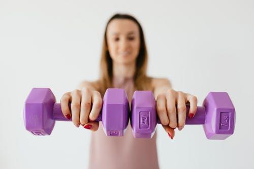 Defocused content young female doing bicep exercise with dumbbells during functional training in light studio