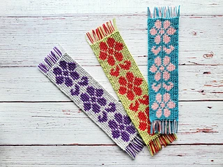 three different colors of tapestry crochet floral bookmarks on white wooden background