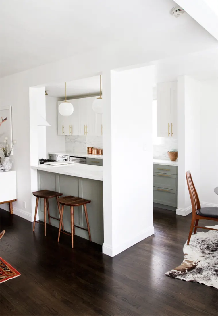 galley kitchen remodel with a large hole cut into the wall, serving as a breakfast nook. white and grey shaker cabinets fill the back wall of the bright modern kitchen