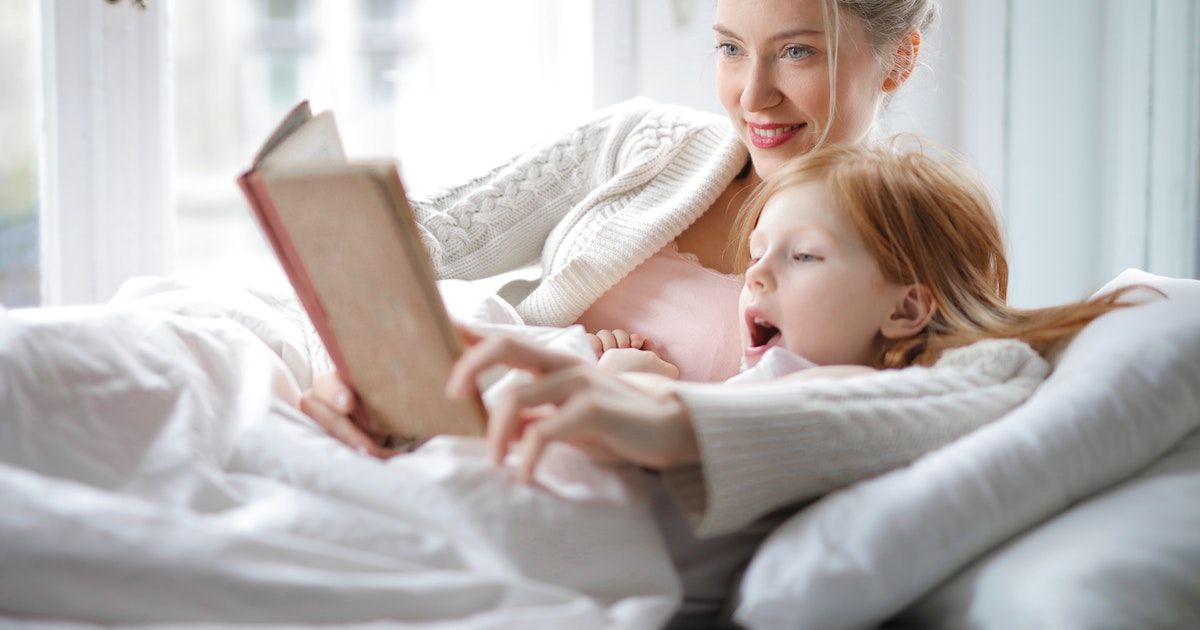 Mother reading book with child under blanket