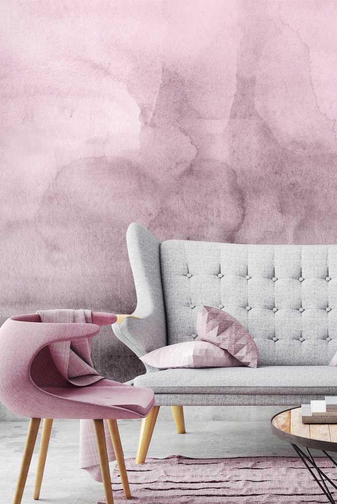 Ambiente com parede de marmorato rosa harmonizando com poltrona e tapete rosa, sofá cinza e almofadas rosa.
