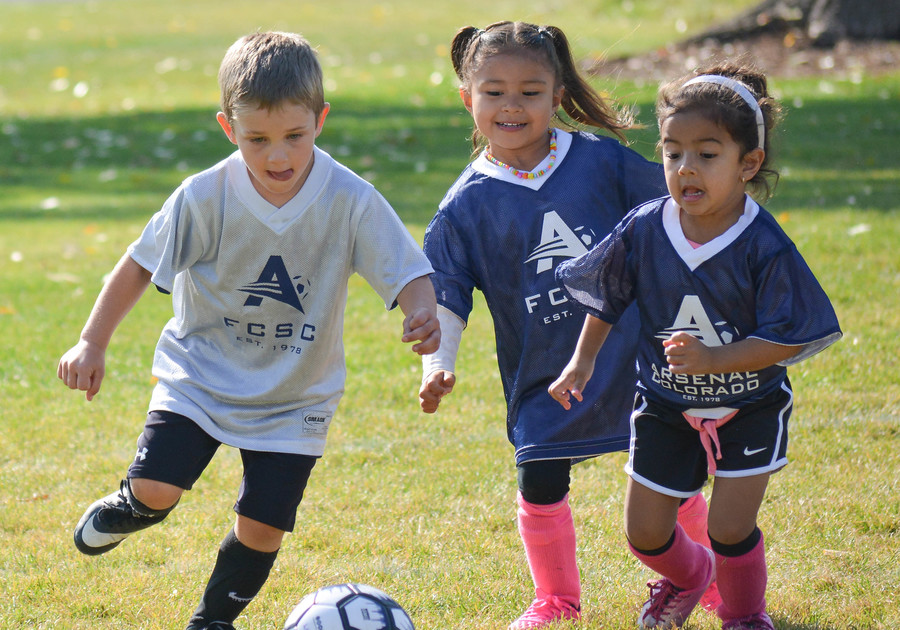 Three children chase a soccer ball in a field at one of Arsenal Colorado’s summer sport camps.