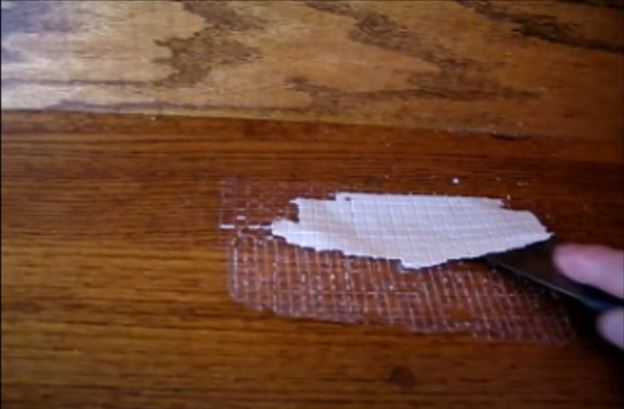 Using a plastic scraper to remove the carpet tape on the wooden floor
