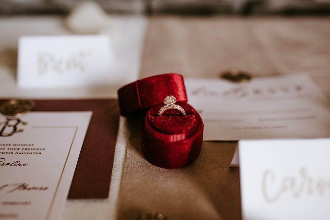 Red box with golden ring placed on table with invitation cards
