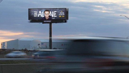 Billboard of a teenager with glasses, and the text "You are not alone" in white behind