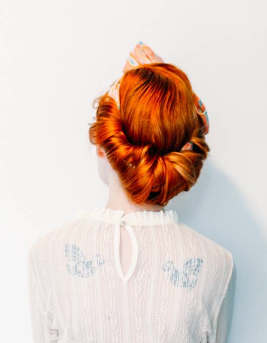 Red headed women wears her hair in a faux chignon, tied with a scarf