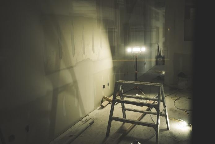 An unfinished room lit by a lamp with a small ladder in the middle.
