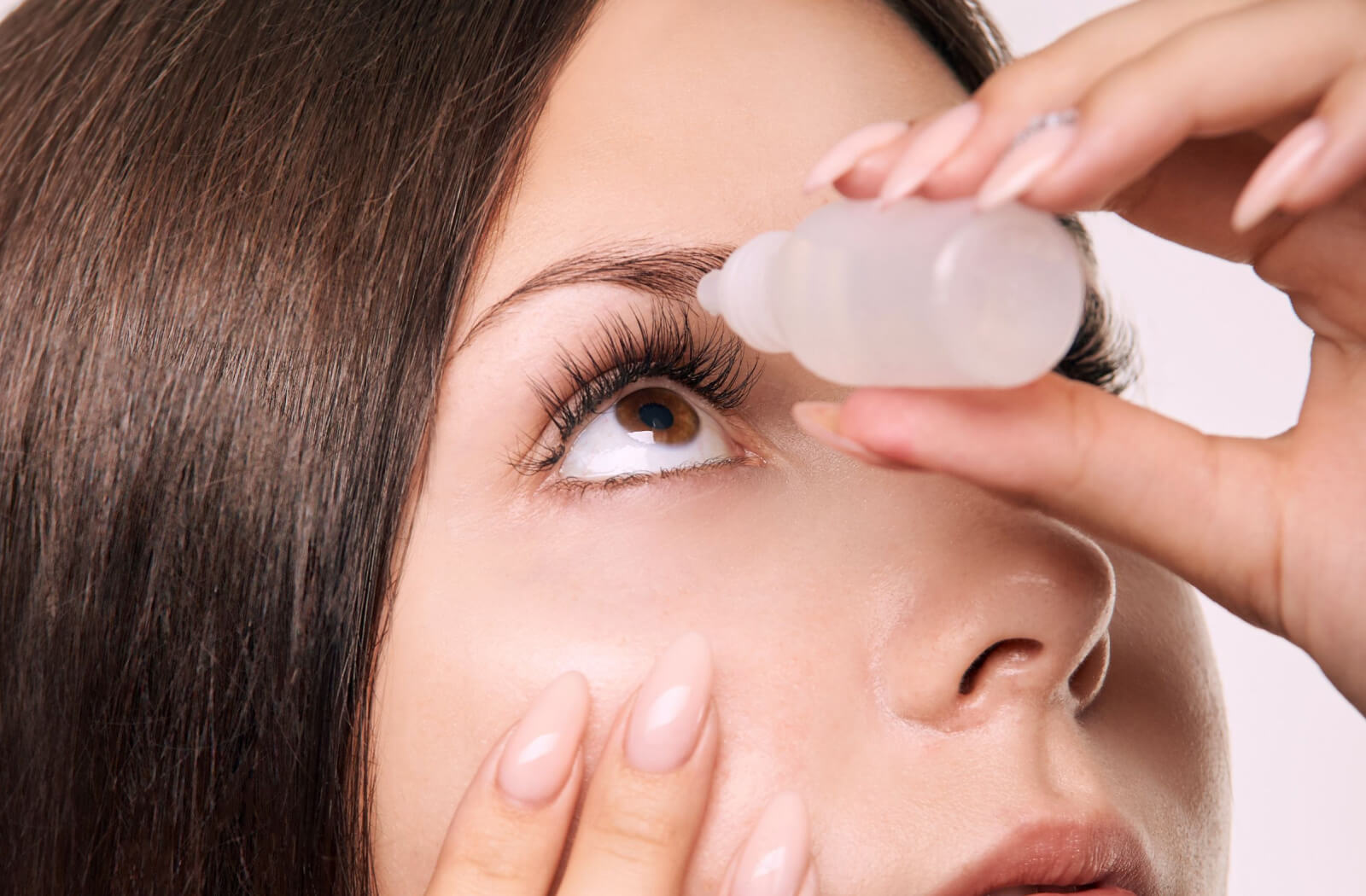 A close-up of a woman pulling her right lower eyelid down to apply atropine eyedrops on her right eye.