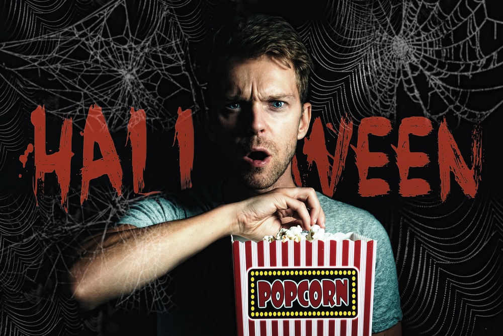 Halloween written in the spiderweb festooned  background of a picture of a man eating popcorn watching a movie