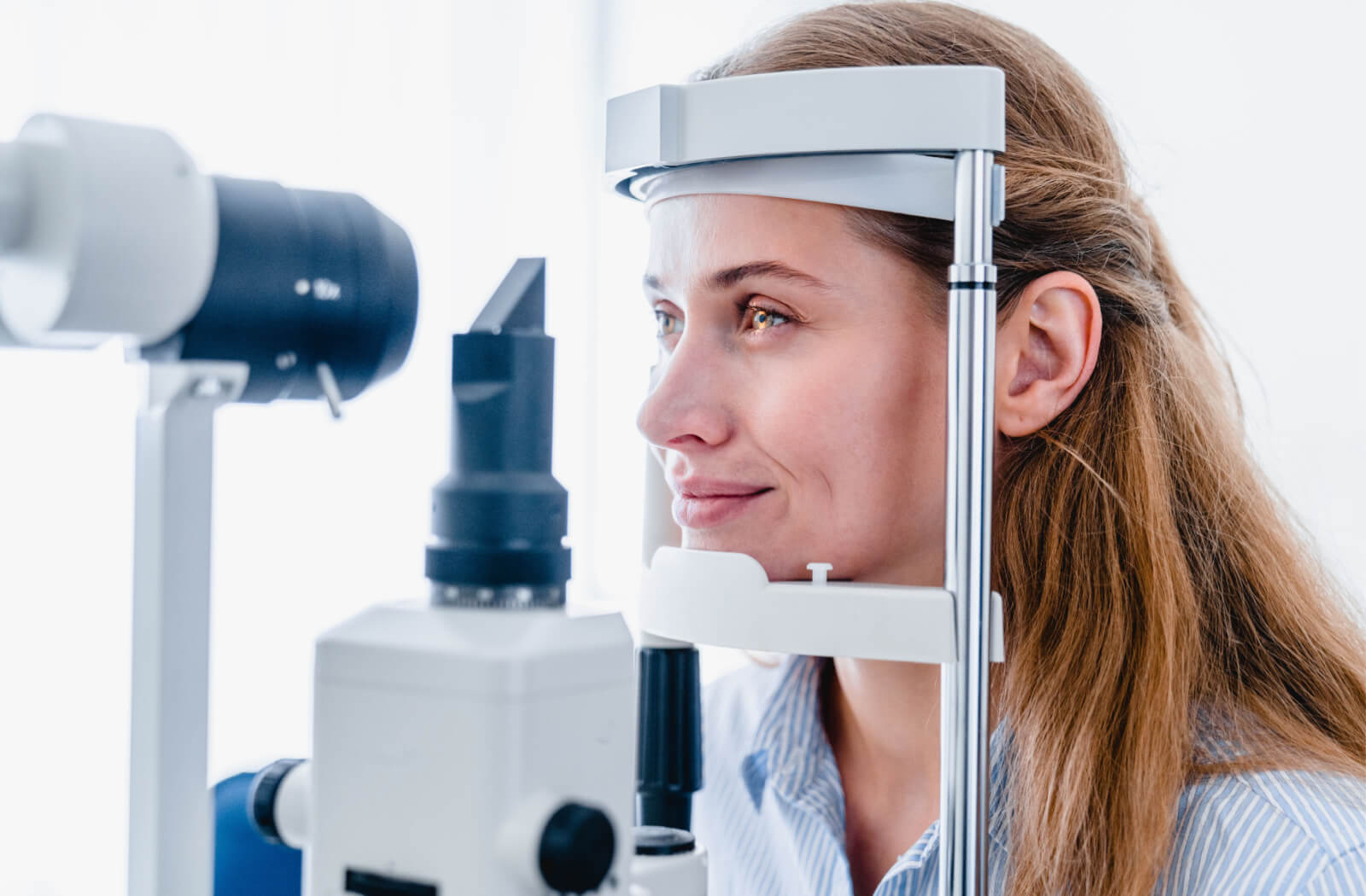 A woman sitting in an optometrist's office looking into a machine that tests her vision.