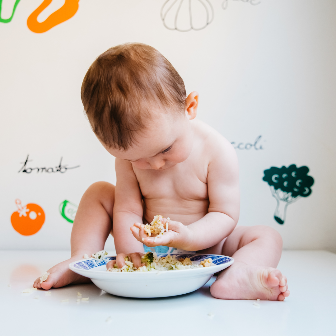 Baby sitting on the floor with his hands in a bowl of rice