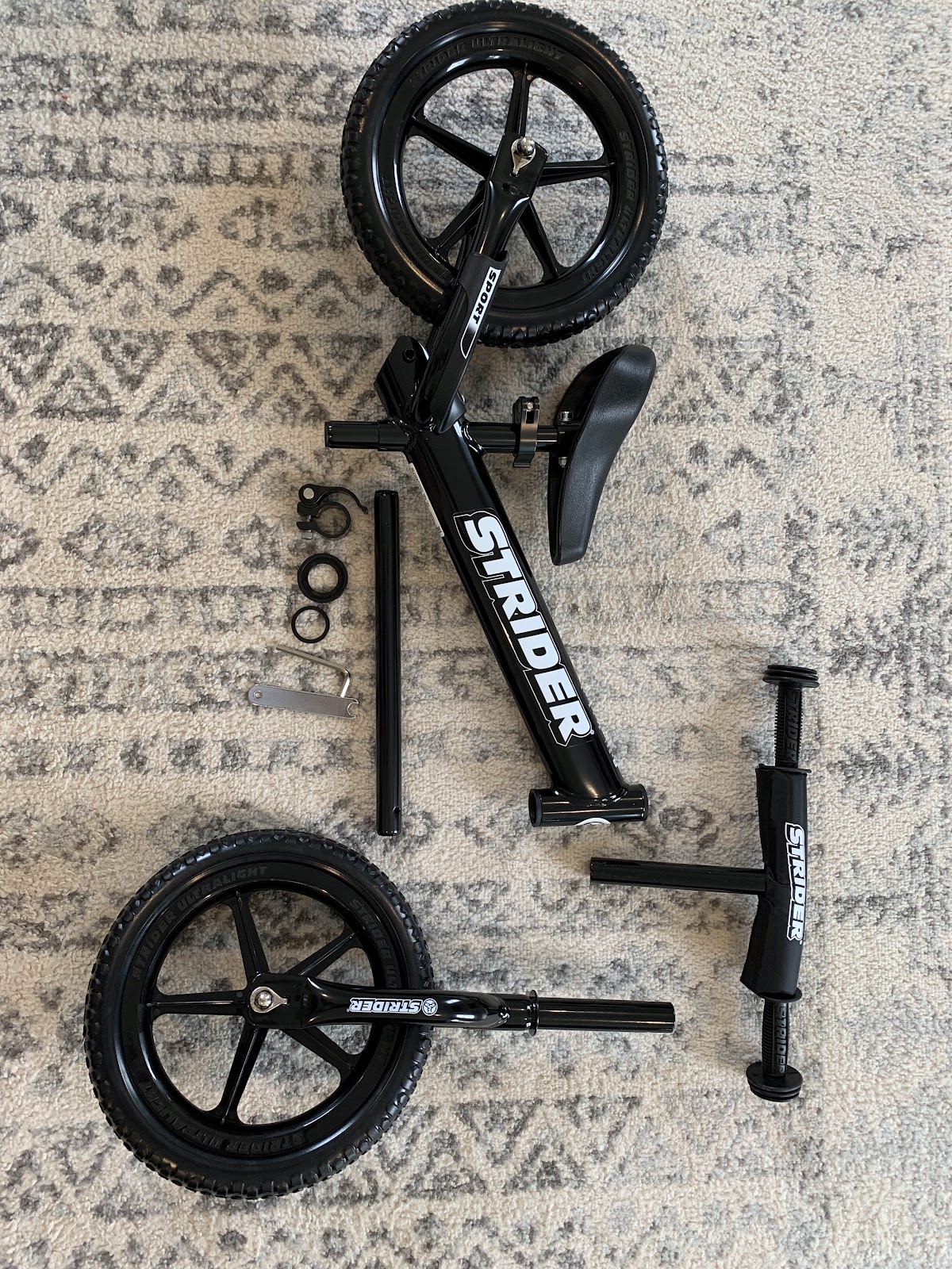 Unassembled pieces of a Strider Bike arranged on a rug