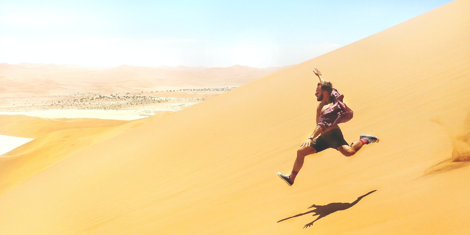 man free running down a large sand dune