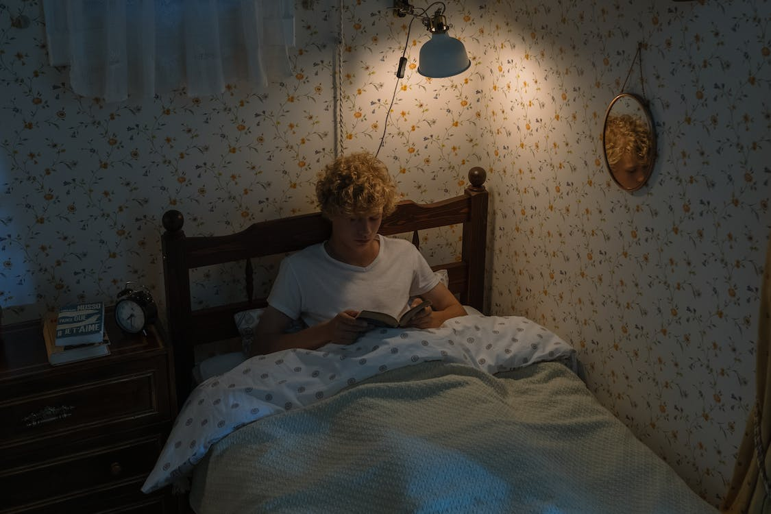 a teenage boy lying in bed and reading
