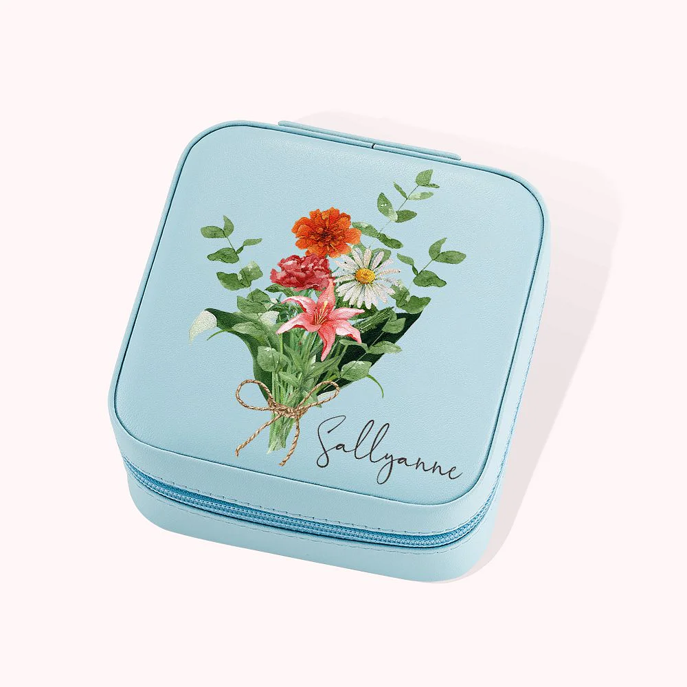 Boîte à bijoux en cuir avec fermeture éclair, de couleur bleue et décorée d’un bouquet de fleurs. Elle est personnalisée par un prénom.