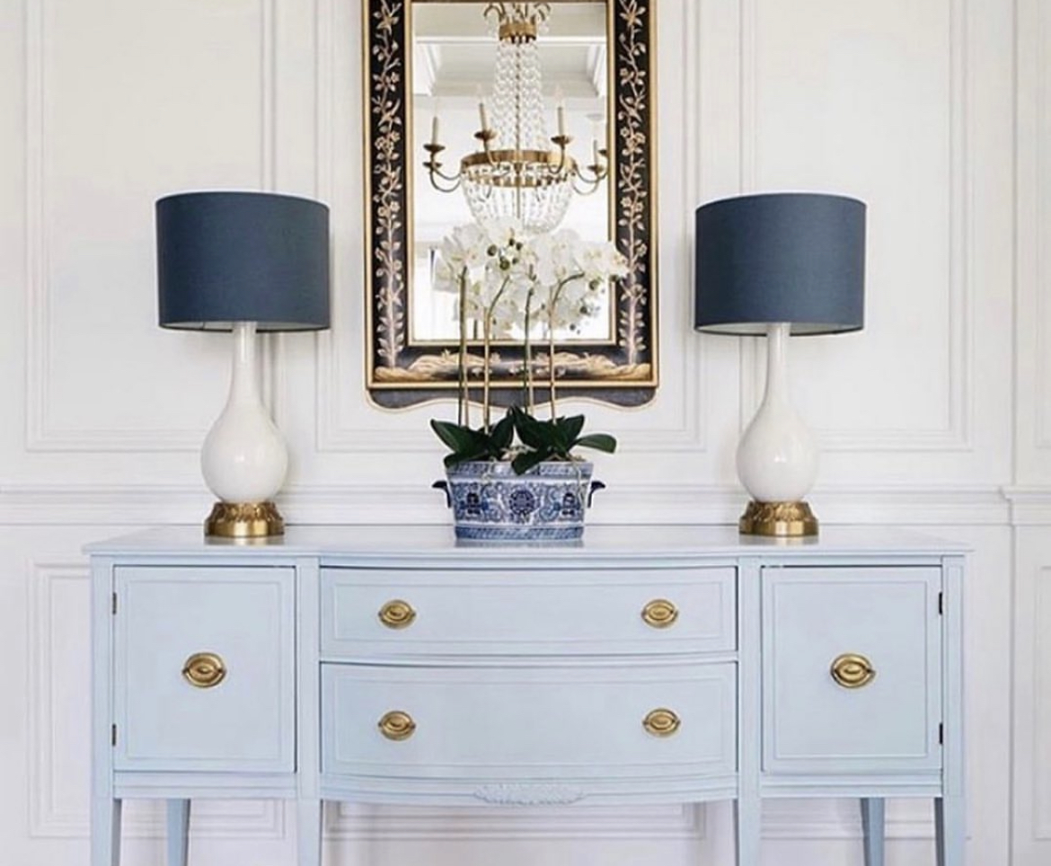 A light blue painted sideboard cabinet adds a pop of color and character to the space and it topped with a pair of lamps, a blue and white porcelain vessel filled with white orchids and a large vertical mirror.Above the cabinet hangs a gorgeous mirror, reflecting the beauty of the room and creating the illusion of more space.This entryway is both practical and stylish, with each piece carefully chosen to enhance the overall look and feel of the space. The result is a welcoming and inviting area that sets the tone for the rest of the home.