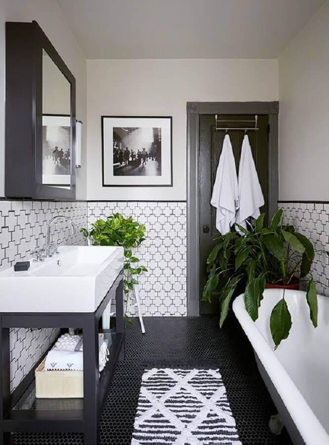 Banheiro com técnica de pintura de meia parede cinza e parede inferior com azulejo branco com desenho preto, piso preto banheira branca, armário e moldura do espelho pretos.