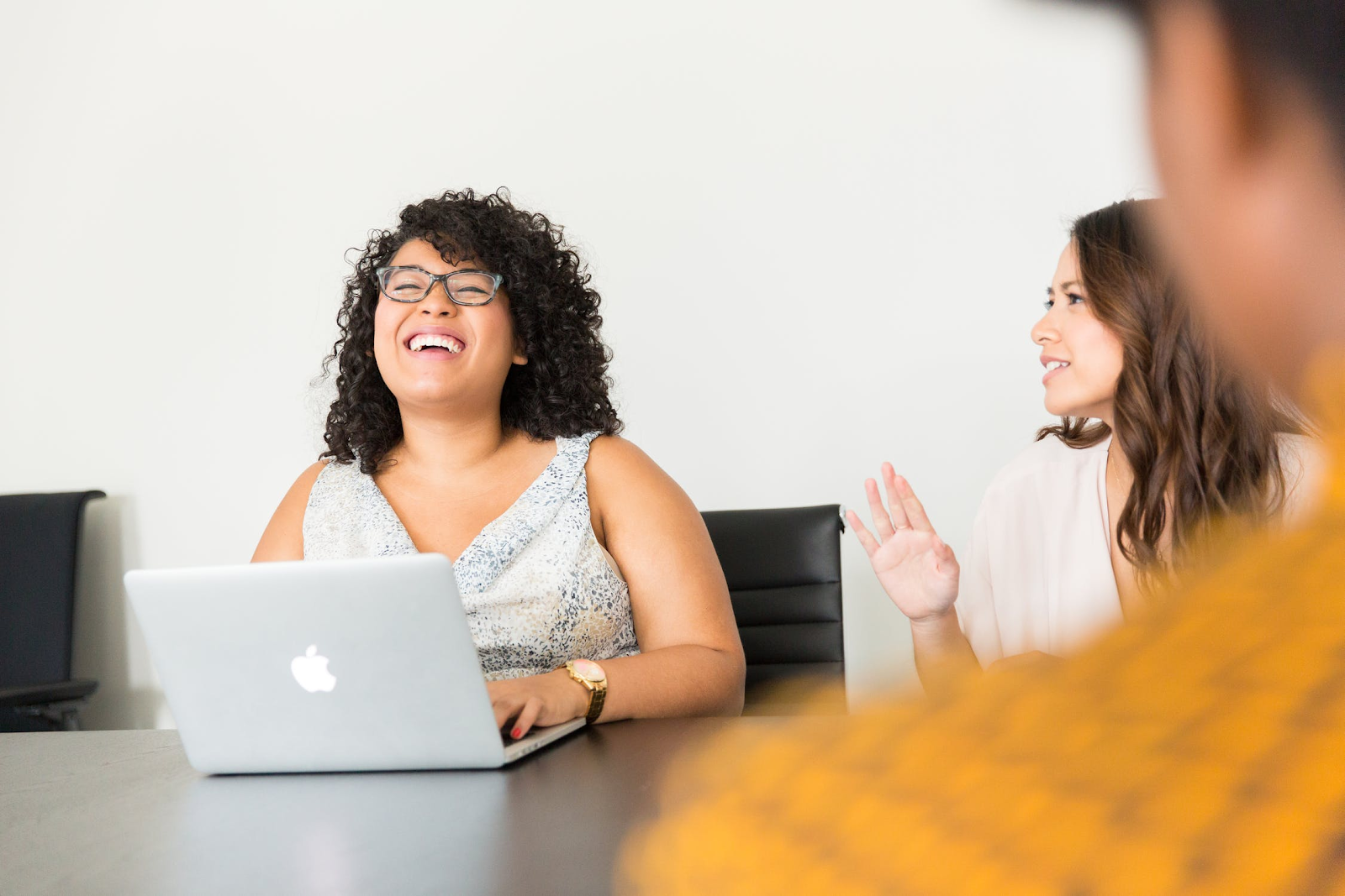 a woman on a laptop laughing at a coworker’s joke