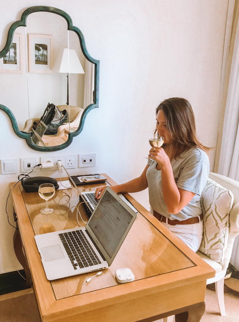 Best places for digital nomads: a girl sips wine while working at her laptop at a hotel desk.