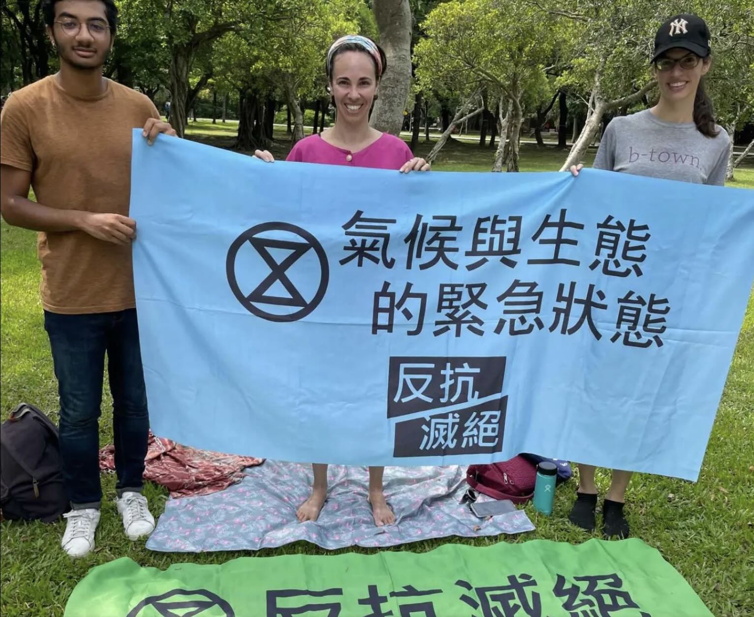 Jen and two other rebels hold up a banner in a public park having done group meditation