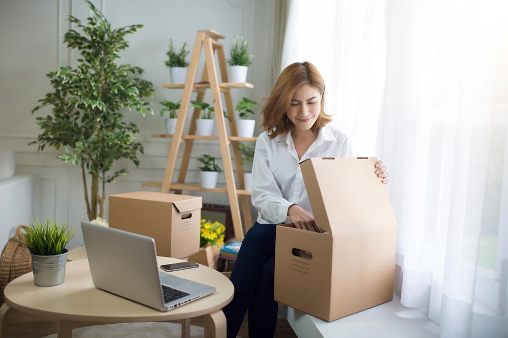 home, post, delivery and happiness concept - smiling young woman opening cardboard box at home,flare light