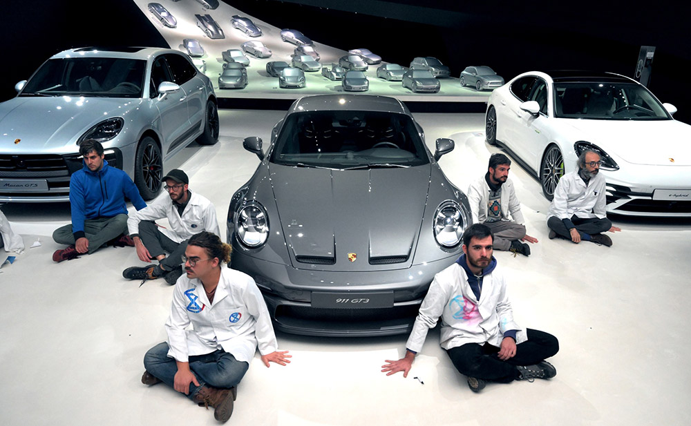 rebels sit around a porsche car, palms glued to the showroom floor