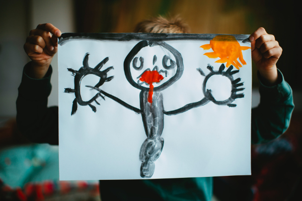 A child holding up a painting of a black figure with the sun in the top right corner.