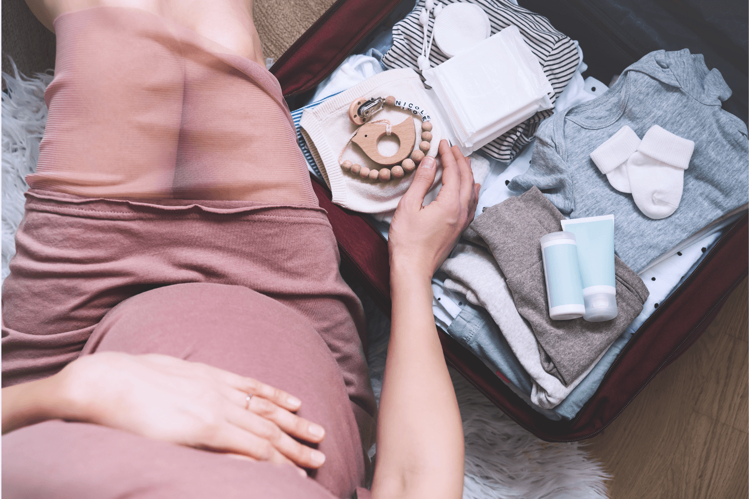 Pregnant mother sitting beside folded newborn clothes and baby accessories