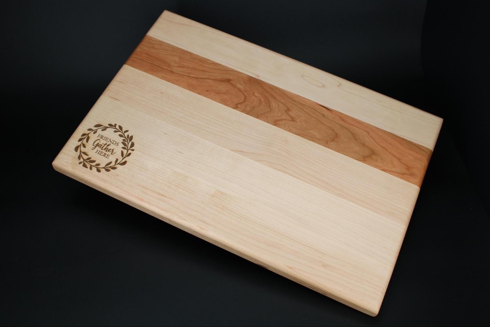 Maple and cherry wood charcuterie board laser engraved with a custom friends gather here wreath