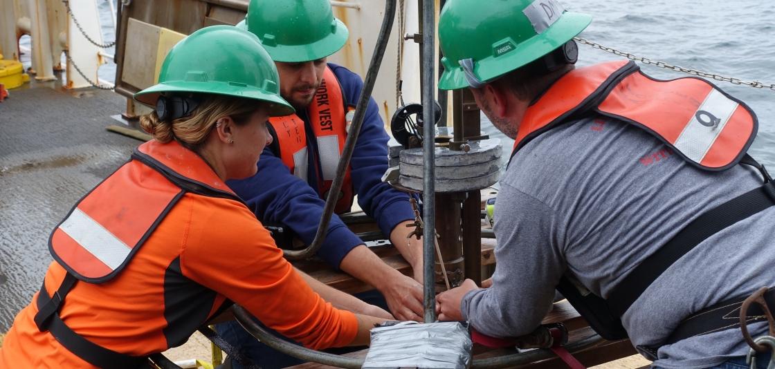 Leslie Irwin (left, NCCOS Silver Spring), Anthony Lima (center, graduate student at University of Texas Rio Grande Valley), and Dave Kidwell (right, NCCOS Silver Spring) carefully remove a core of sediment collected by the Craib corer from the bottom of the Gulf of Maine.