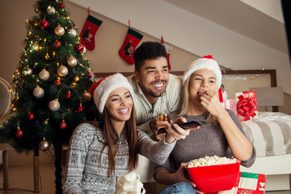 a group of people in santa hats eating popcorn on the couch and smiling while watching something on tv 