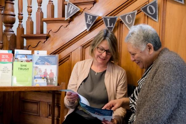 Two people are looking at a brochure, a sign above says 'welcome'