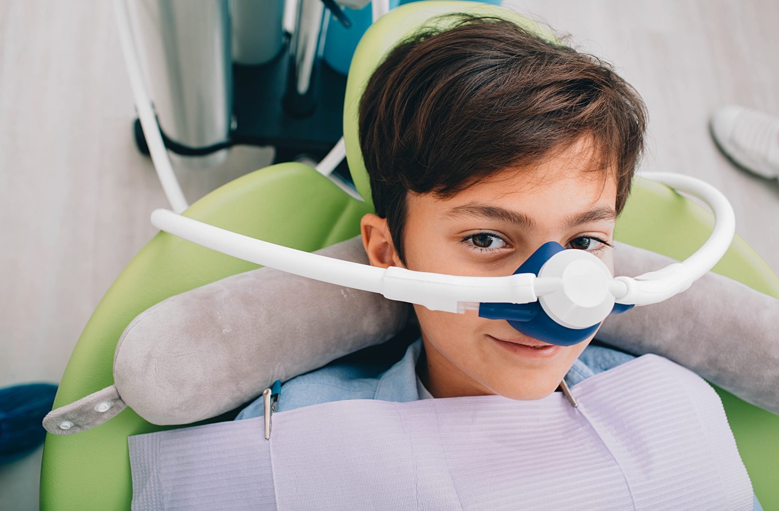 Little boy sitting in a green dentist's chair receiving inhaled sedation through a blue and white mask