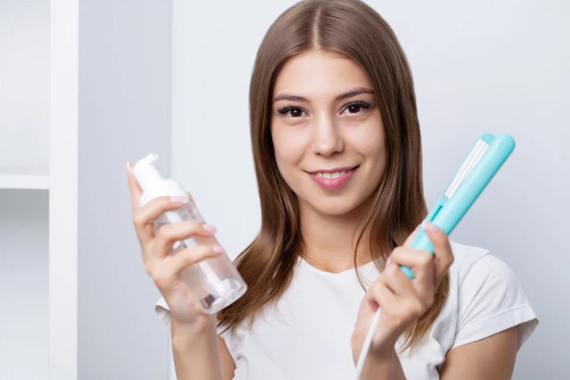 Mulher segurando produto de cabelo e uma chapinha