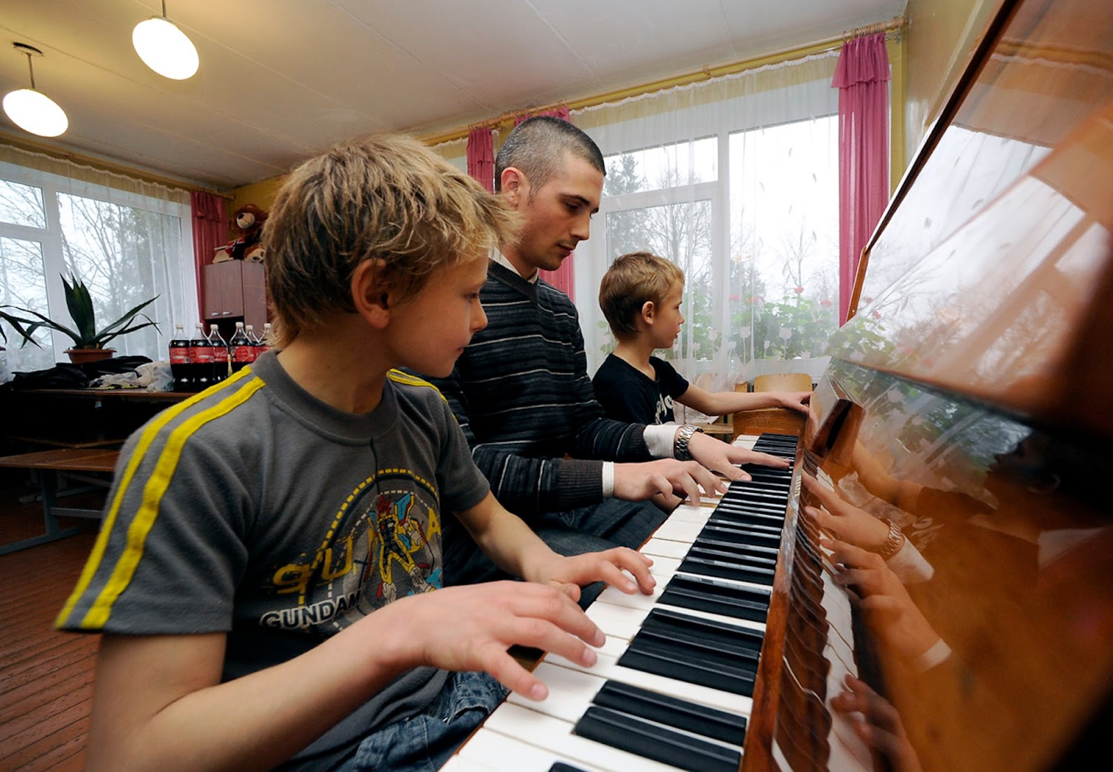 A tutor teaching two kids how to play the piano