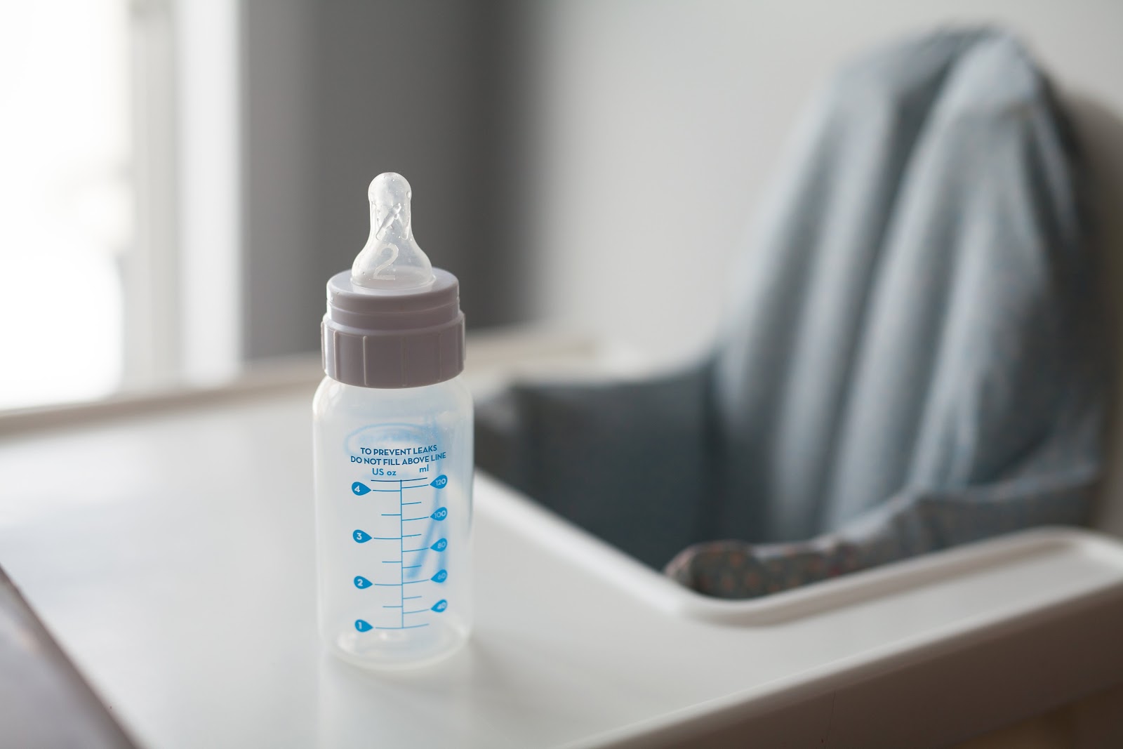 empty baby bottle, used to feed baby formula to a baby, placed on a high chair