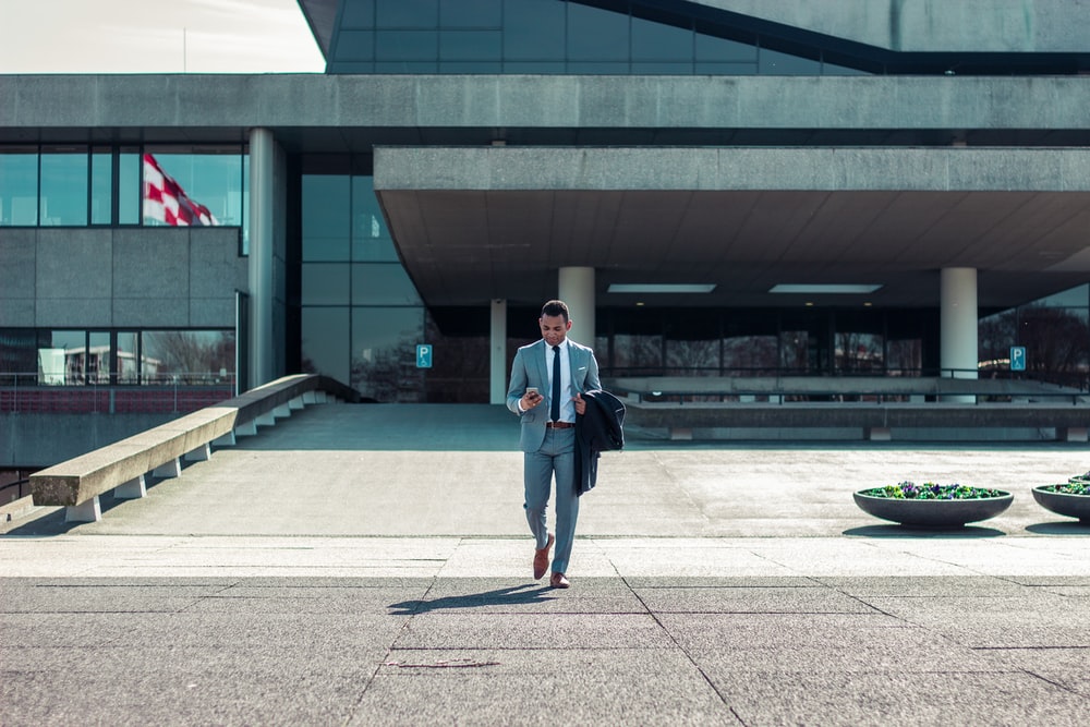 Man walking in front of office building while holding black coat