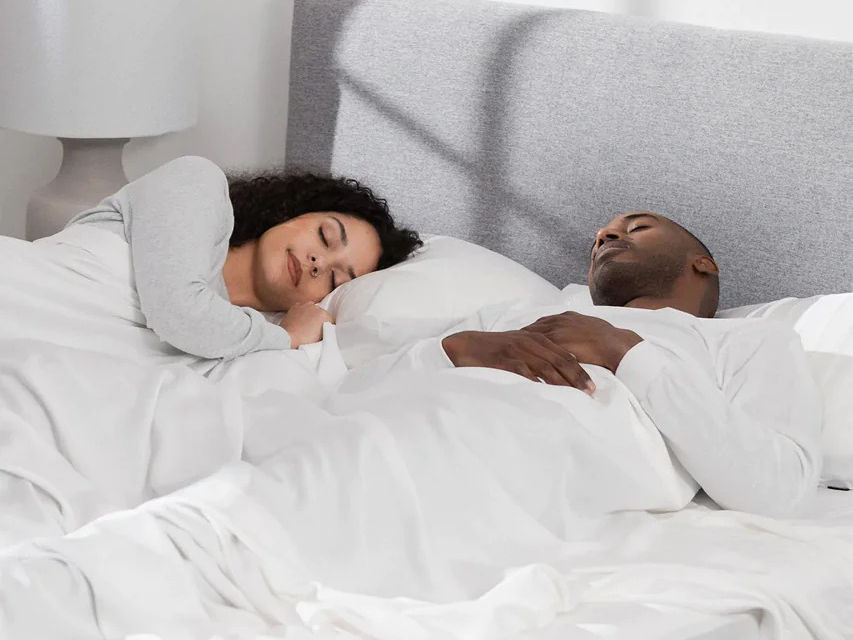 A couple sleeping under a set of white Hush sheets.