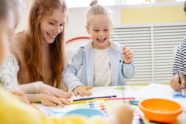 teacher and little girl smiling over paper and paints